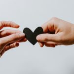 A hand passing over a support love heart to another hand with a peach colour overlay