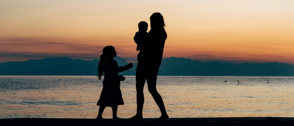 A black and white silhouette photo of a mother caring for her son and daughter on the beach.